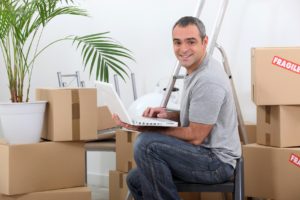 Man using a laptop computer sitting amongst cardboard boxes